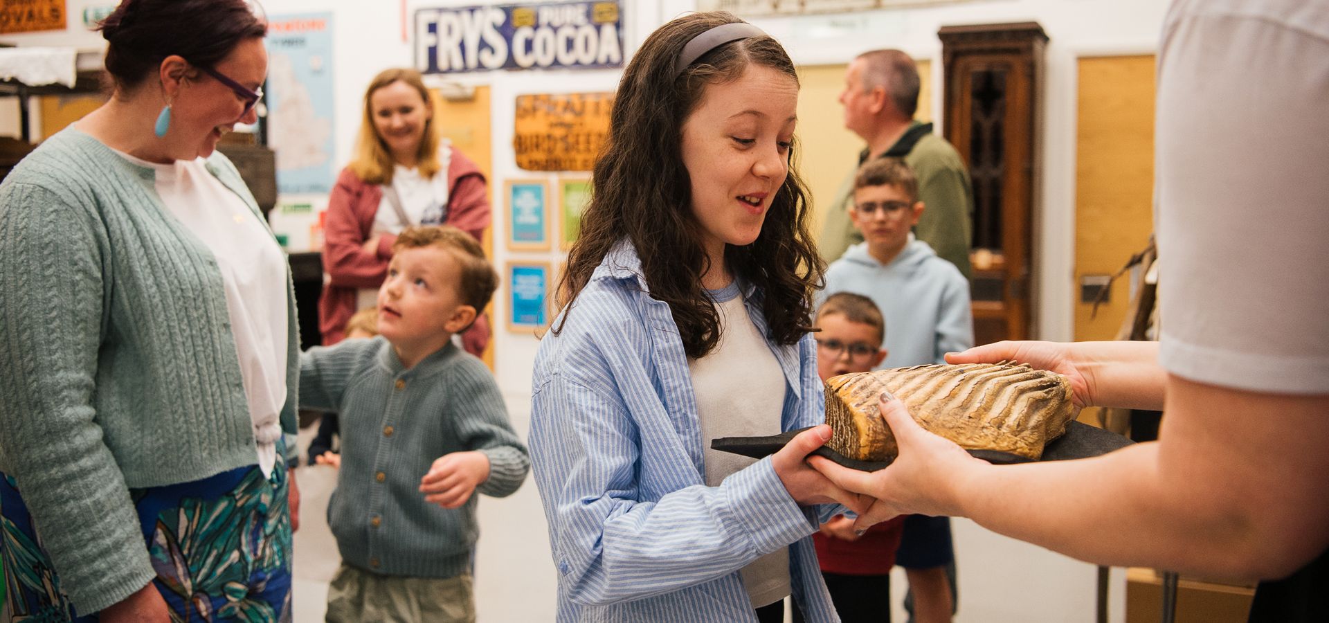 A teenager feeling a fossil being held by a curator with people waiting behind