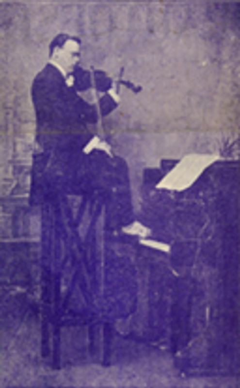 A black and white image of Mark William Dearlove  playing a violin sat on a stool, playing the piano with is feet