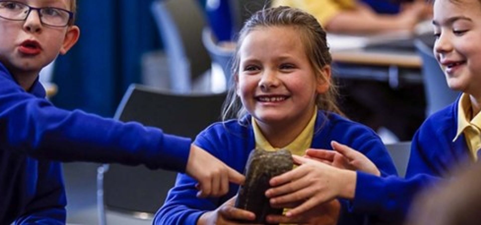 School pupils smiling as they get to hold on to an artefact from the collection.