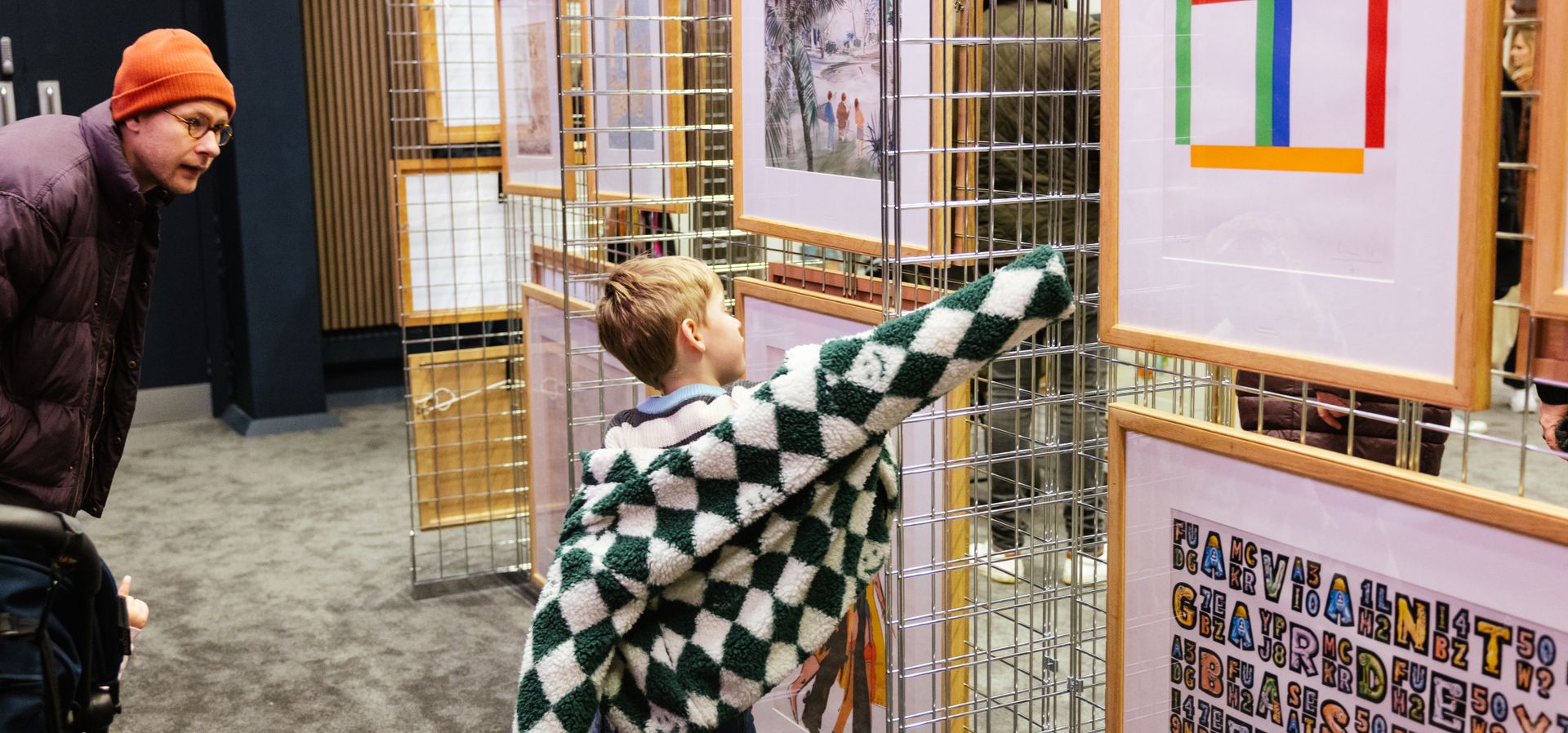 An adult and child looking at framed art on a wire pop-up wall
