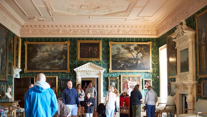 A number of people visiting Temple Newsam in a highly decorated room with lots of paintings and fine furniture on display.