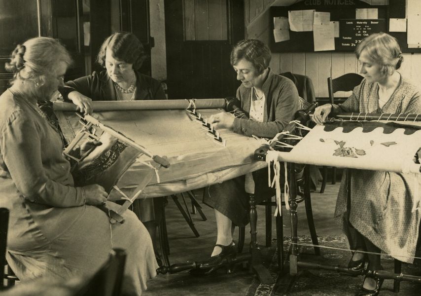 A black and white image of 4 women sat on chairs sewing