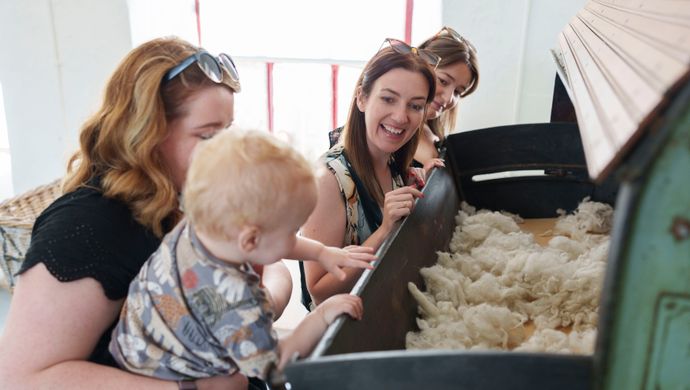 3 adults and a toddler looking into a industrial machine with wool in