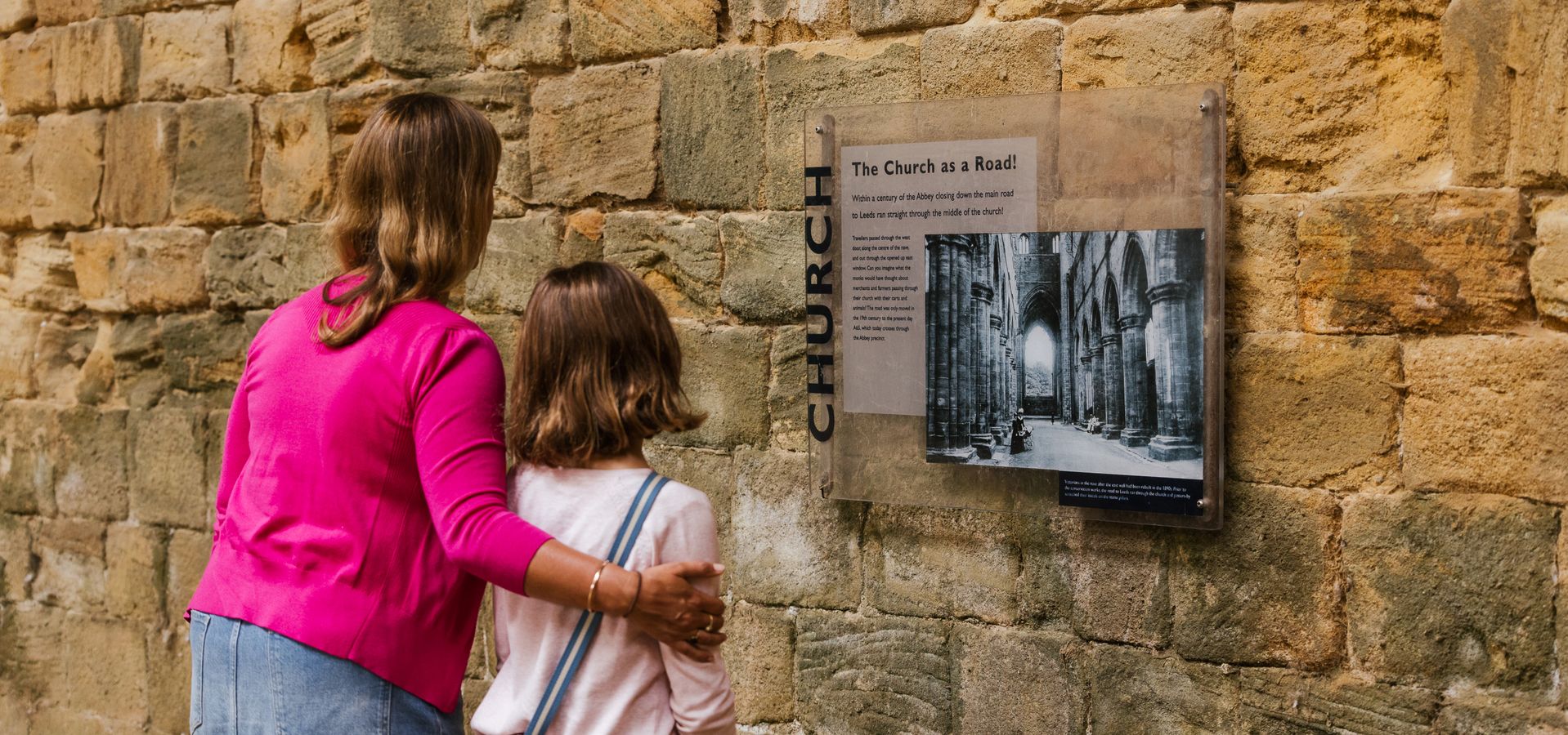 a woman and child looking at interpretation on a wall in the abbey