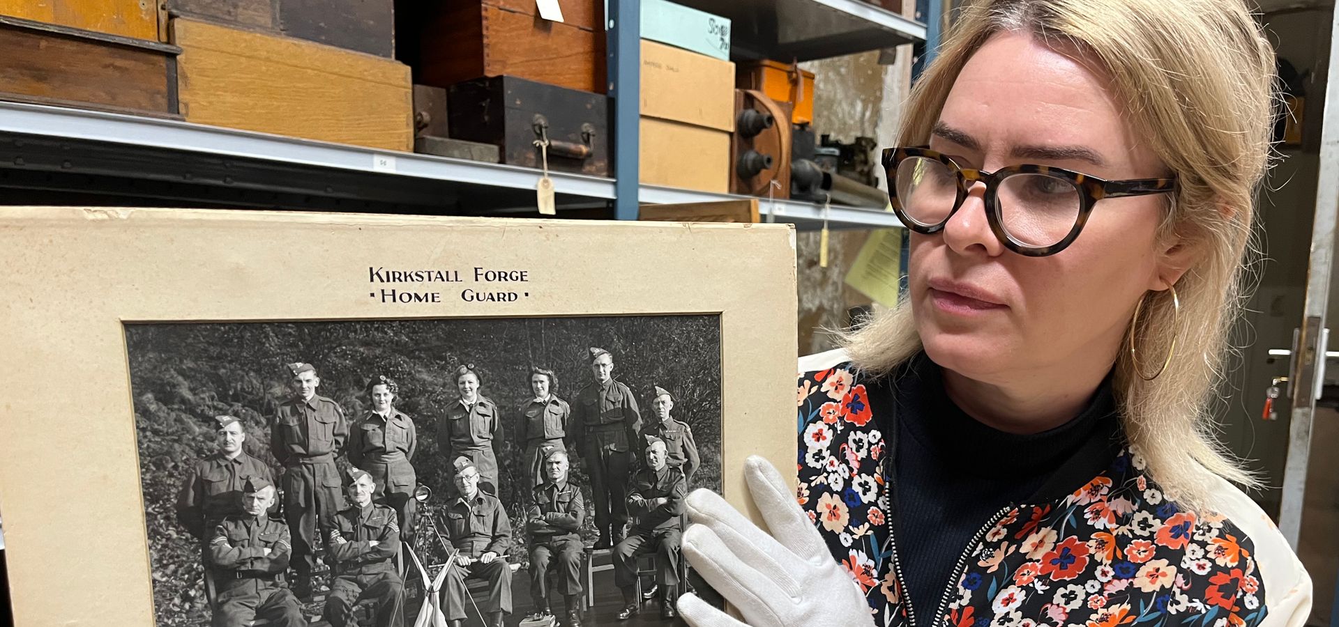 A curator holding a black and white image of 12 men and women from Kirkstall Forge Home Gaurd