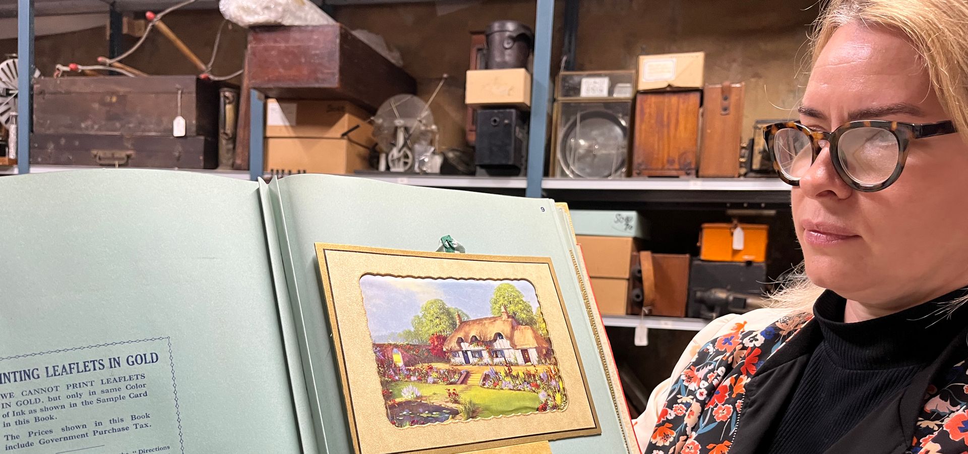 A curator holding a book with a thatched roof house on