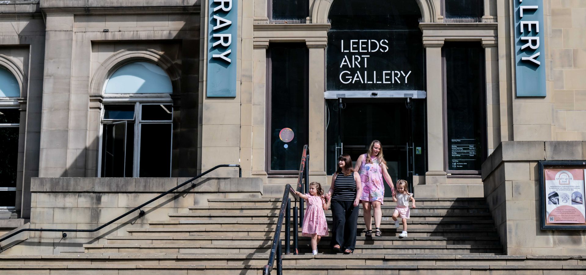 two adults and two children walking down steps in front of Leeds Art Gallery