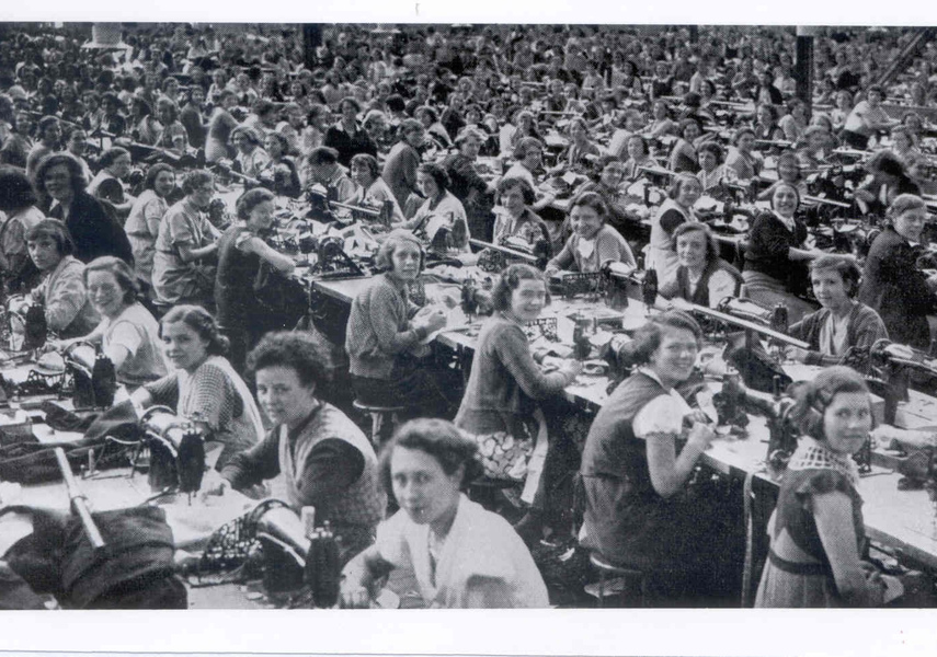 Large room full of women sitting benches working on sewing machines