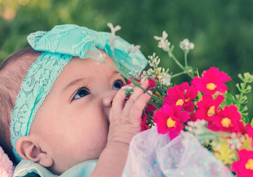 A baby is photographed with flowers whilst laying on grass.