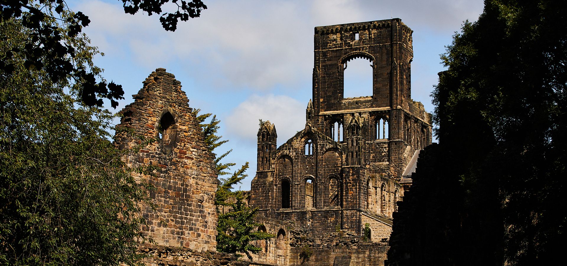 A view of Kirkstall Abbey ruins through trees