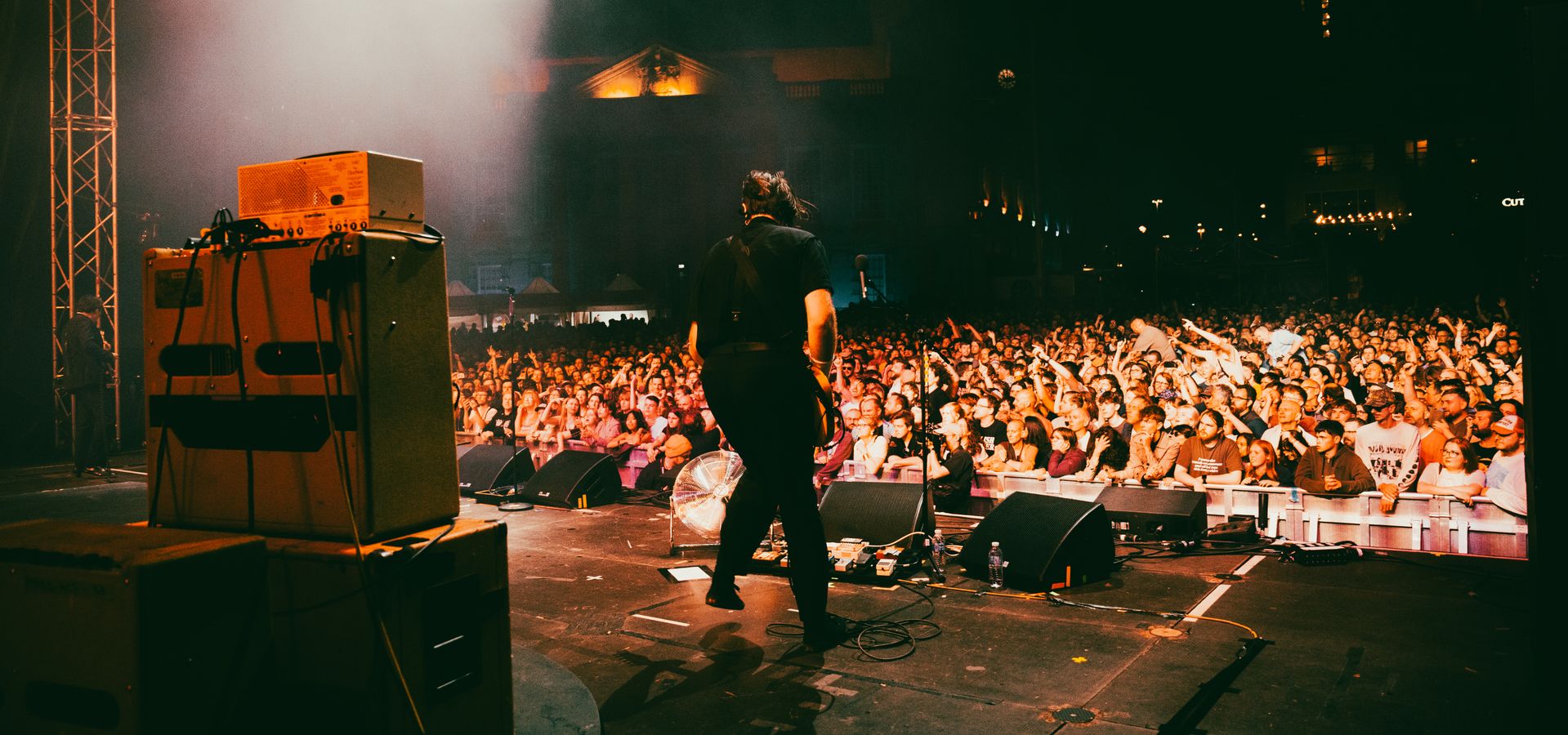 An artist playing music on a big stage during a concert with a crowd in the background