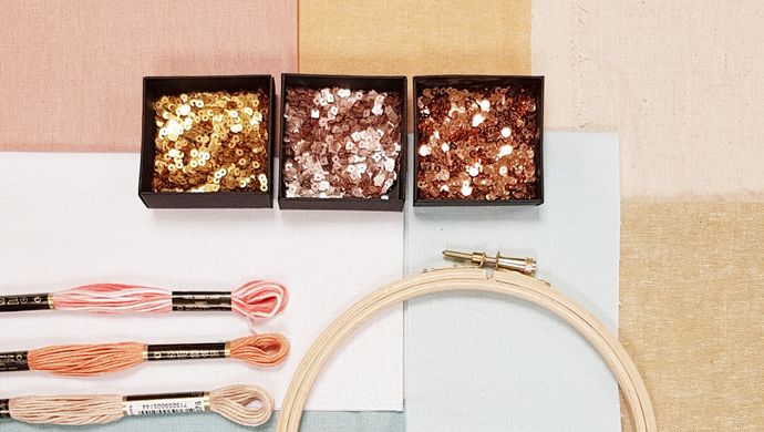 A hand-stitch frame with 3 pieces of coloured thread and packets of sequins on patchwork fabric