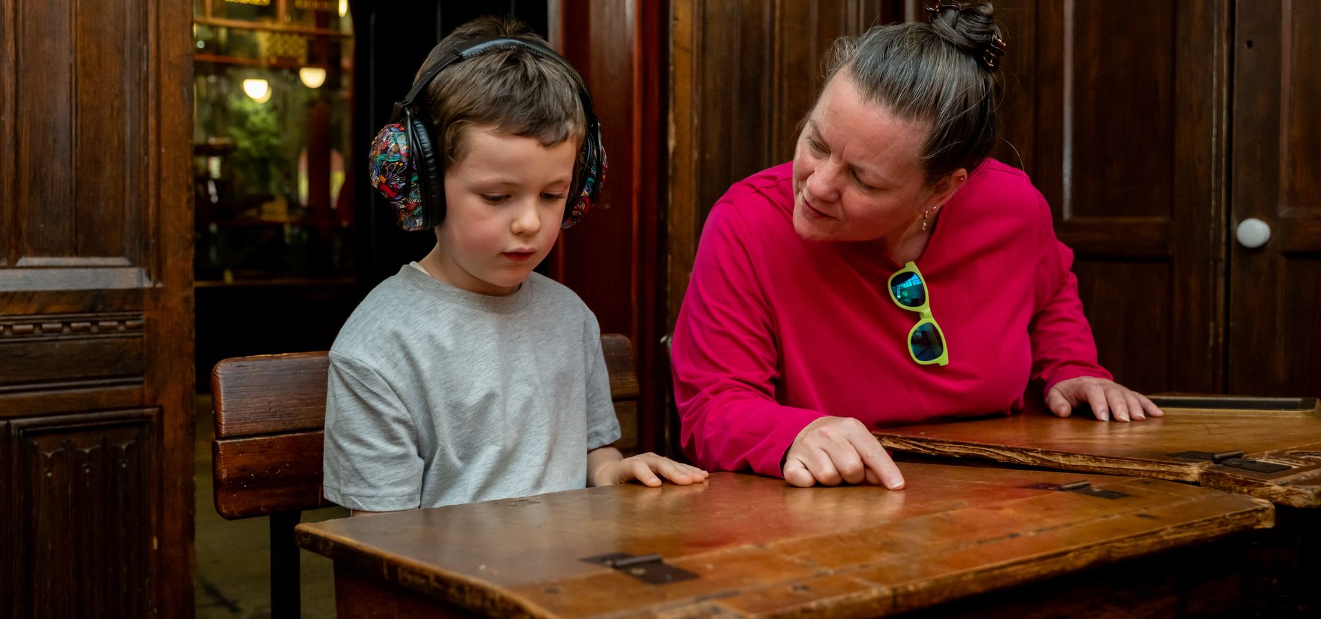 An adult and child sat at an old fashioned school desk