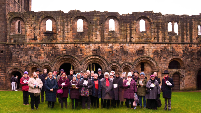 A choir group stood on grass with Kirkstall Abbey behind