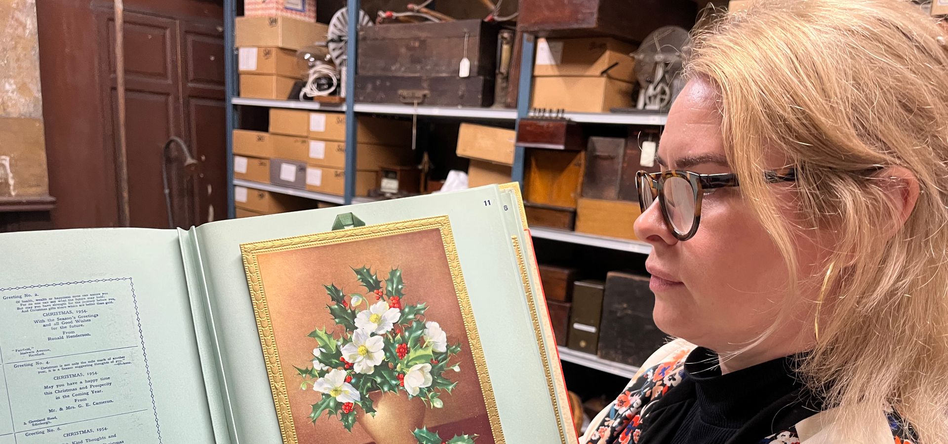A curator holding a book with a winter vase with holly and white flowers in