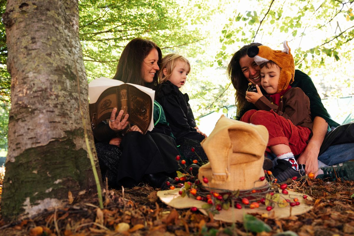 Two adults and 2 children sat in a woodland in a sack and some books