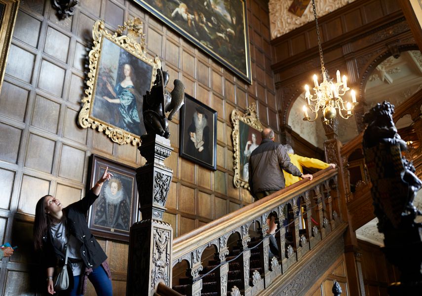 A wooden staircase and a wood panelled wall with framed paintings, inside Temple Newsam House.