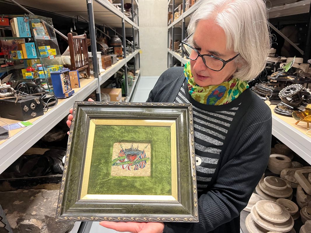 Curator Kitty Ross with the decorated biscuit from 1914, beautifully painted with an image of a battleship and carrying an inscription that reads ‘Wishing you a Merry Christmas and a bright new year’. 