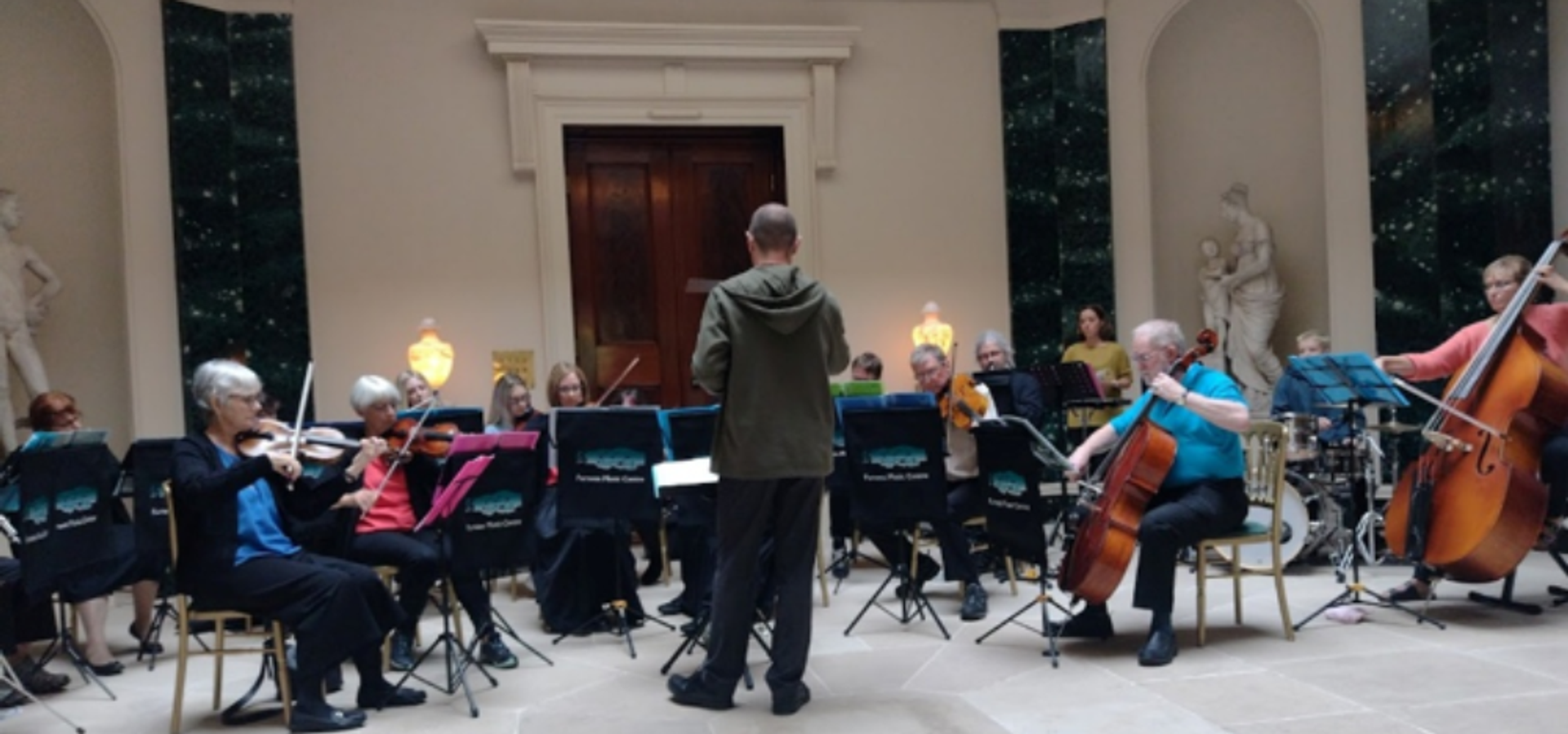A conductor stands in front of a small orchestra with string instruments