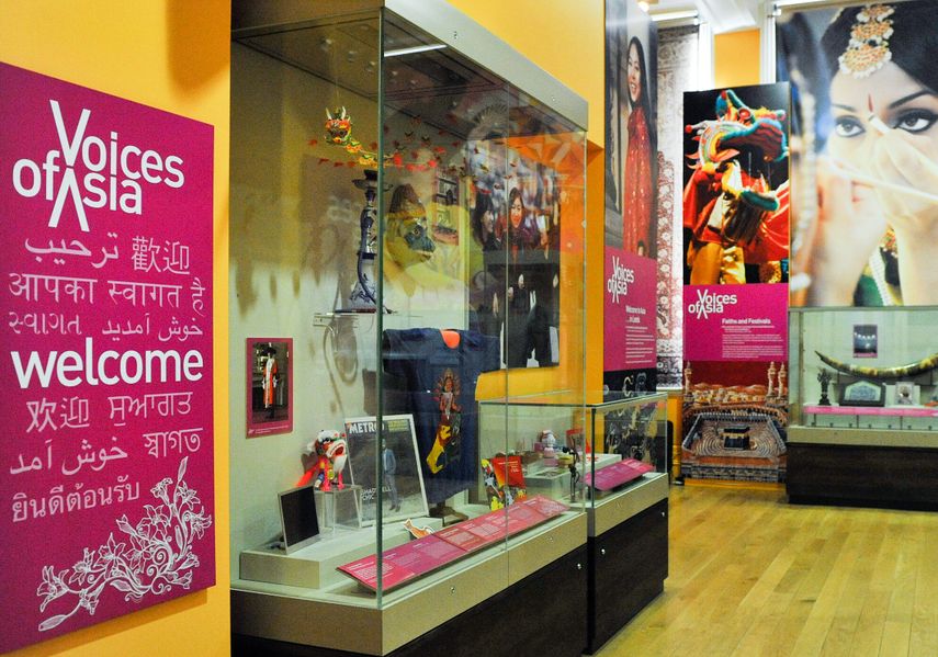 A red sign with voices of Asia on and Welcome in English and different Asian languages, with display cabinets of objects