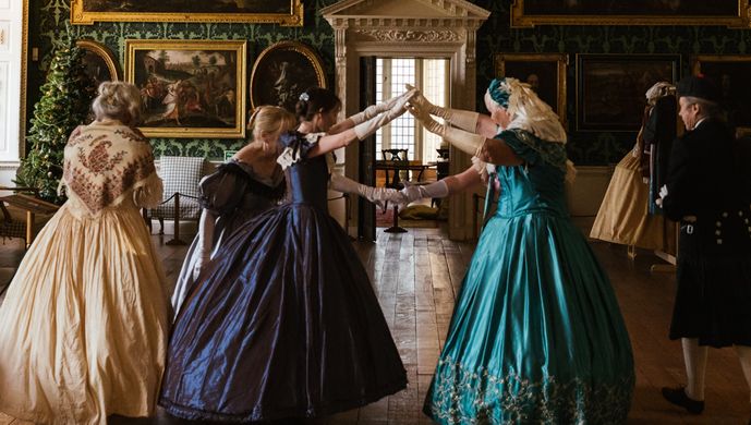 A group of dancers in long dresses with their arms reached up to make a tunnel