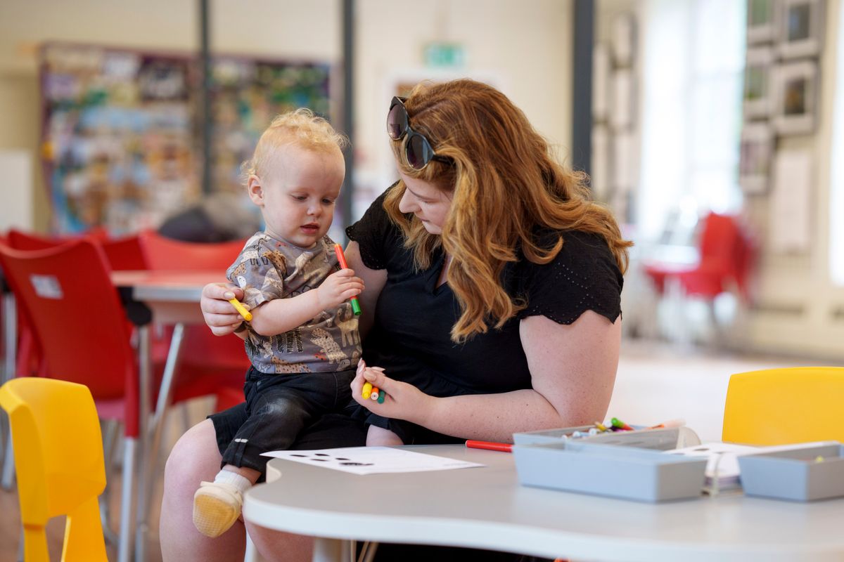 A toddler sat on a woman's knee holding craft pens