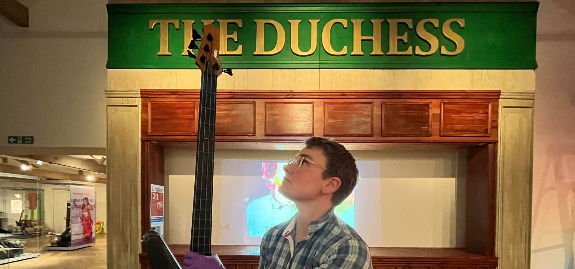 A curator holding a gituar in front of a pub sign 'The Duchess'