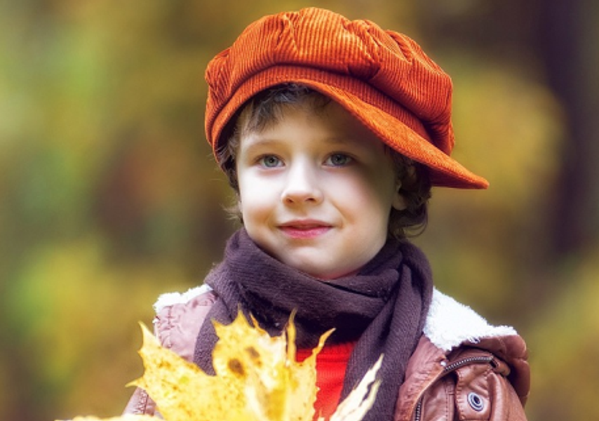 A young boy in an orange hat holding leaves, walking around orange bushes.