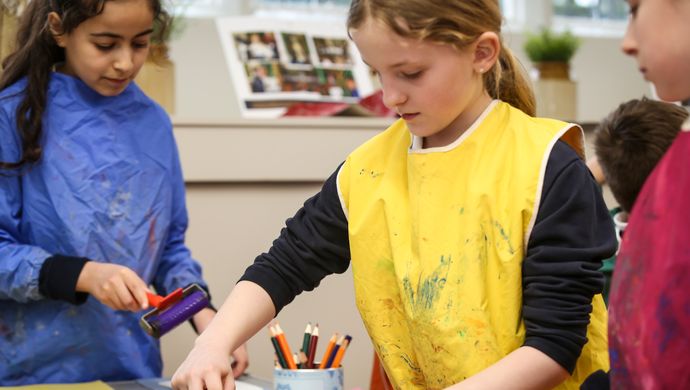 Children wearing aprons using printing rollers to create art