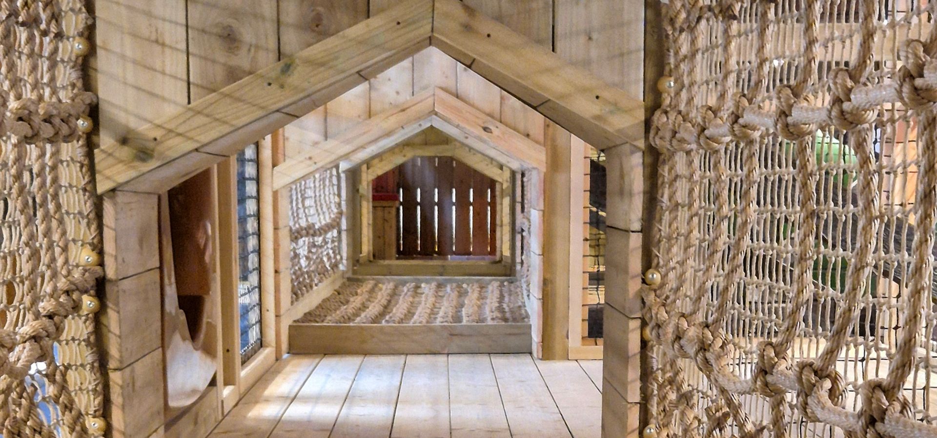 A wooden tunnel playarea with a rope bridge