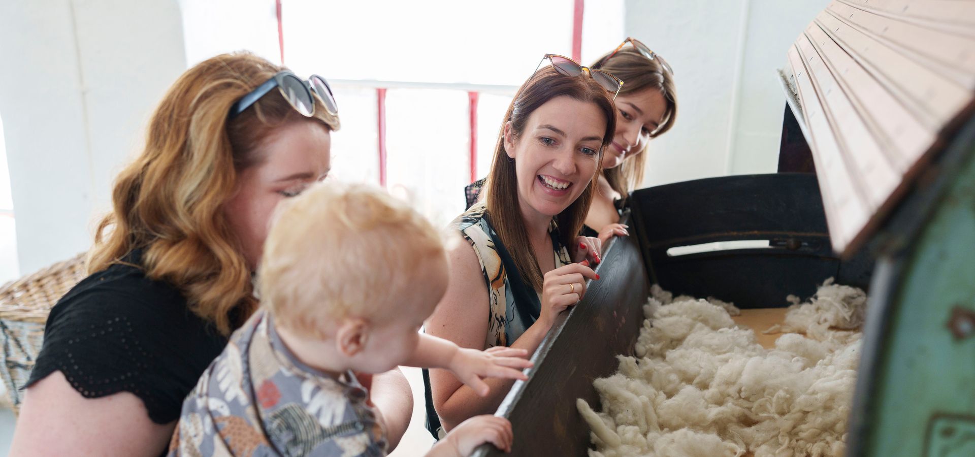 3 adults and a toddler looking into a industrial machine with wool in