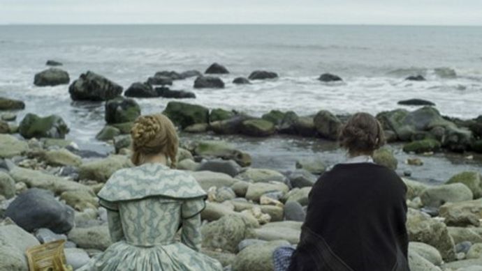 two women in 19th century costume sitting on a beach