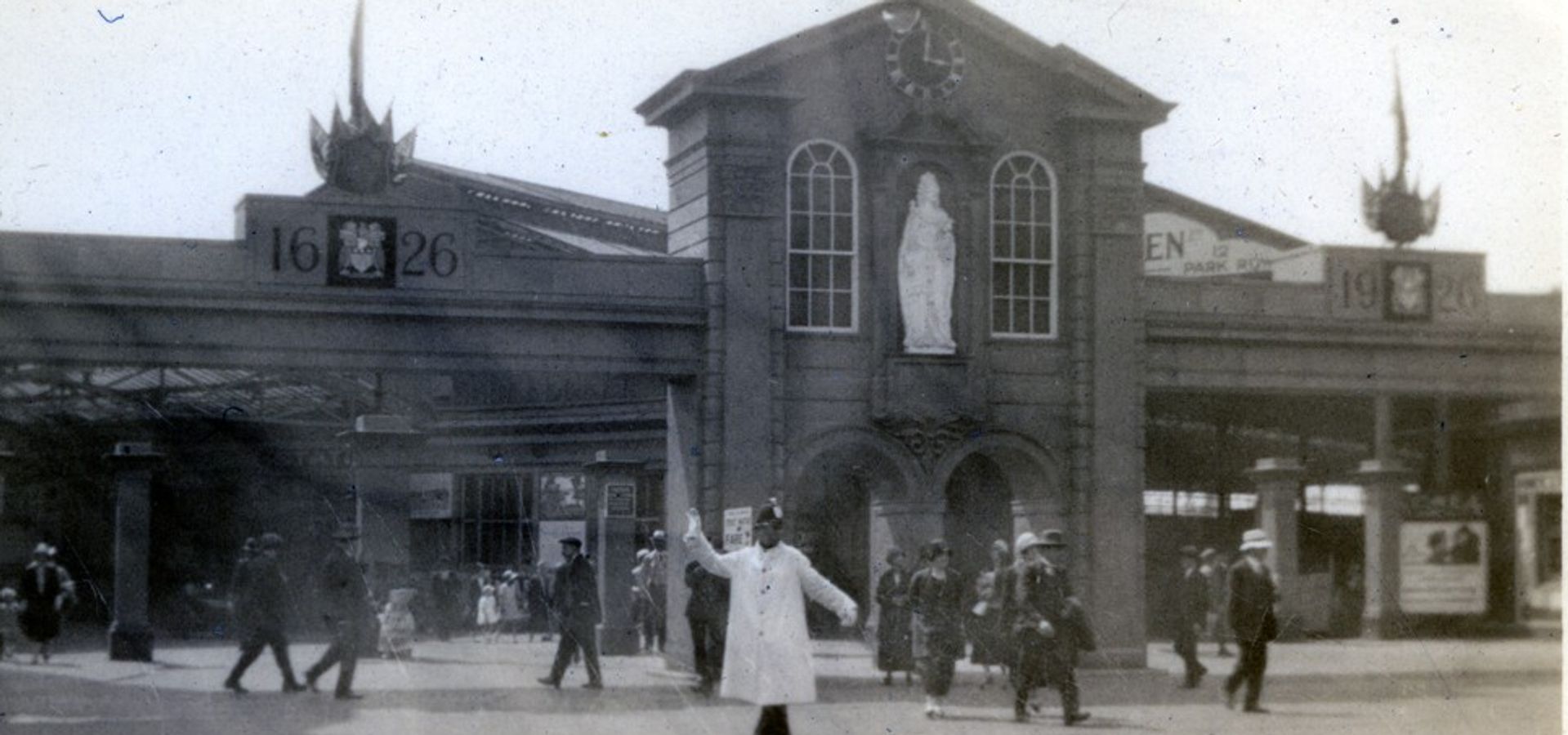 A black and white image from 1626 of a building in Leeds with a person in white walking across ringing a bell