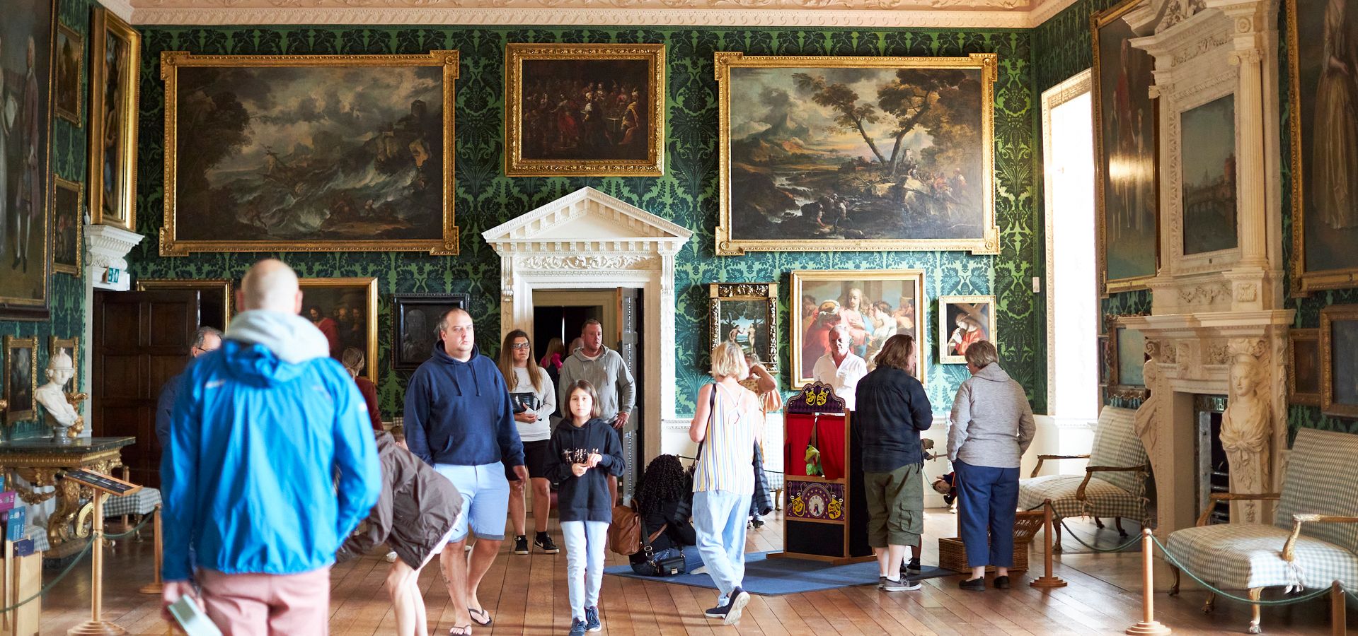 A number of people visiting Temple Newsam in a highly decorated room with lots of paintings and fine furniture on display.