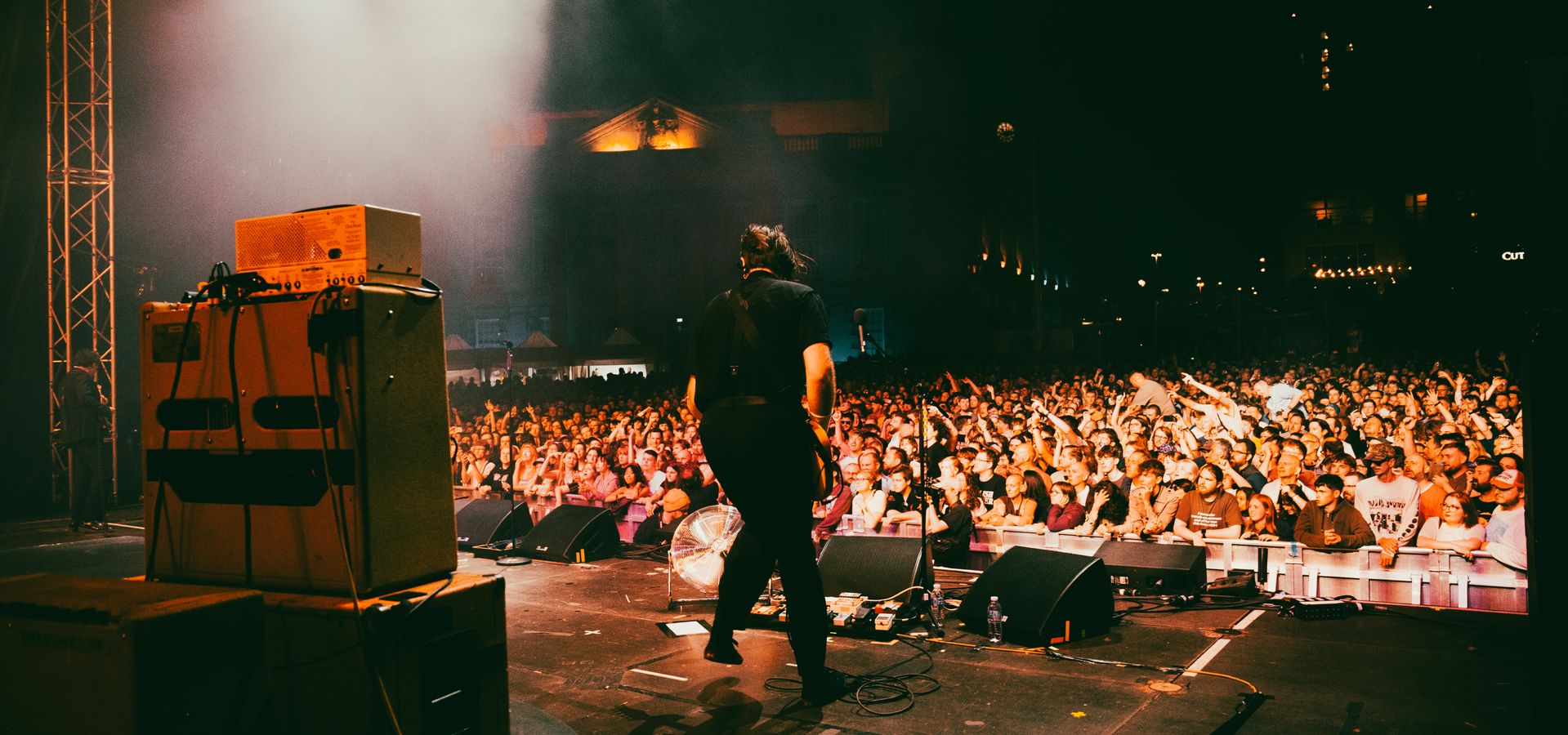 An artist playing music on a big stage during a concert with a crowd in the background