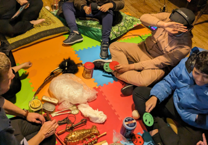 A group of young people sit on cushions surrounded by sensory objects during a sensory workshop.