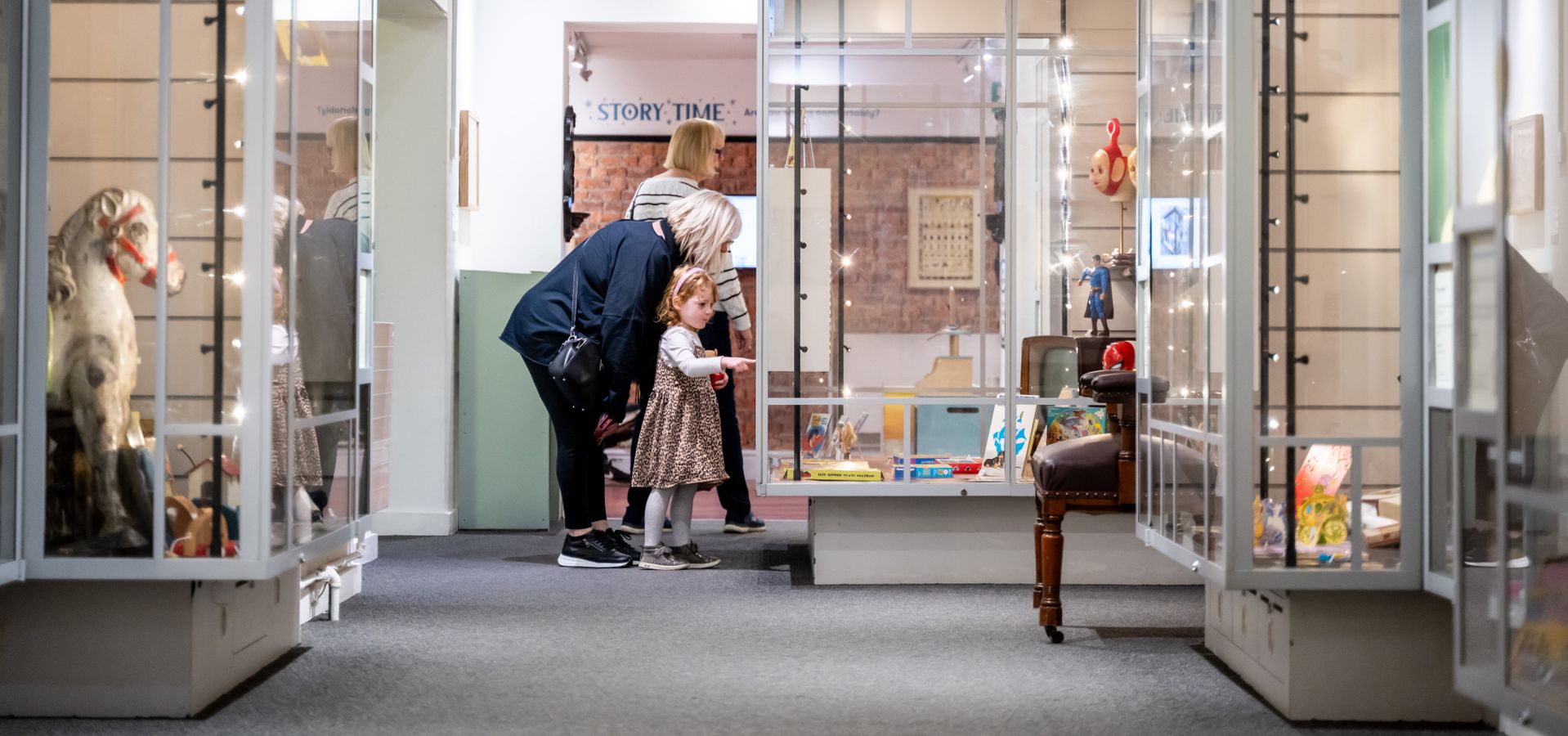 A child and 2 adults looking into exhibition cabinets upstairs in Abbey House Museum